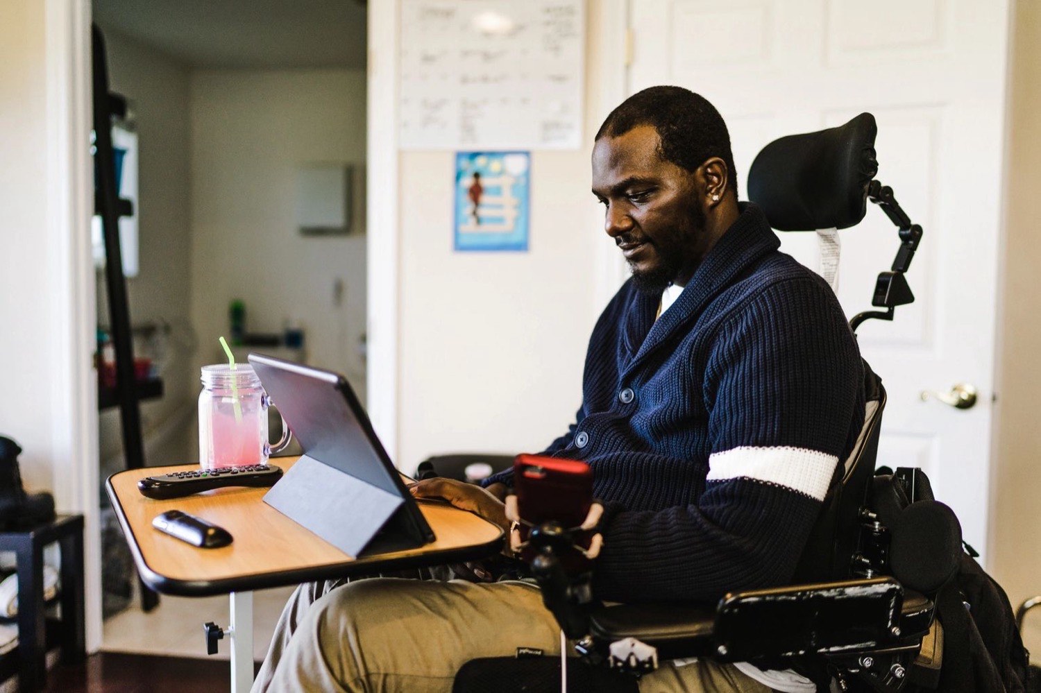 A man using a power wheelchair working at a tablet in his home