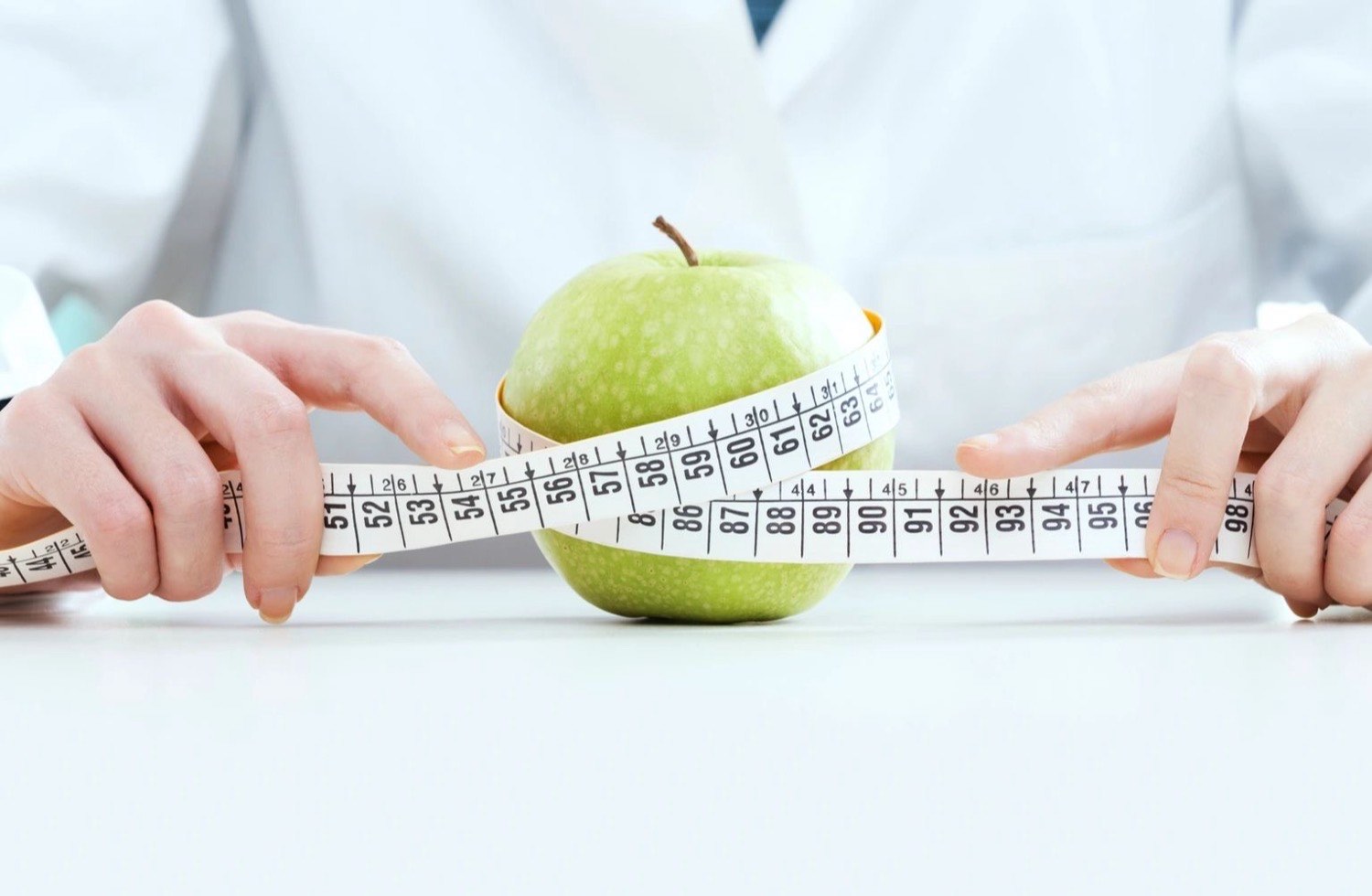 A health professional holding a green apple wrapped in a measuring tape