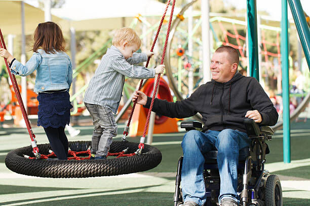 A carer and a child together on a swing set outdoors